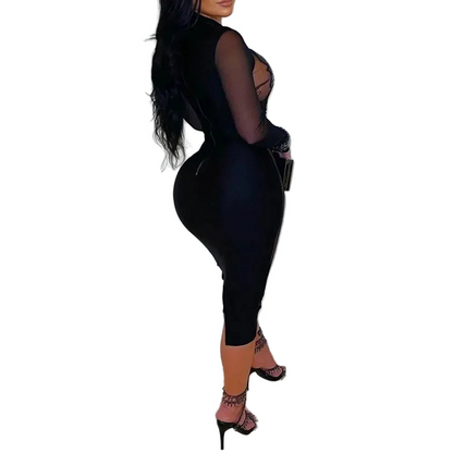 Woman wearing a black outfit with sheer panels against a white wall.