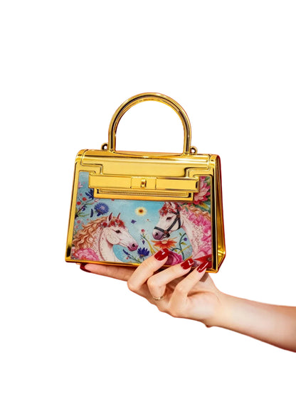 Hand holding a gold handbag with a colorful unicorn design against a red background